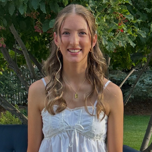 A young woman in a white top poses alongside a wicker chair